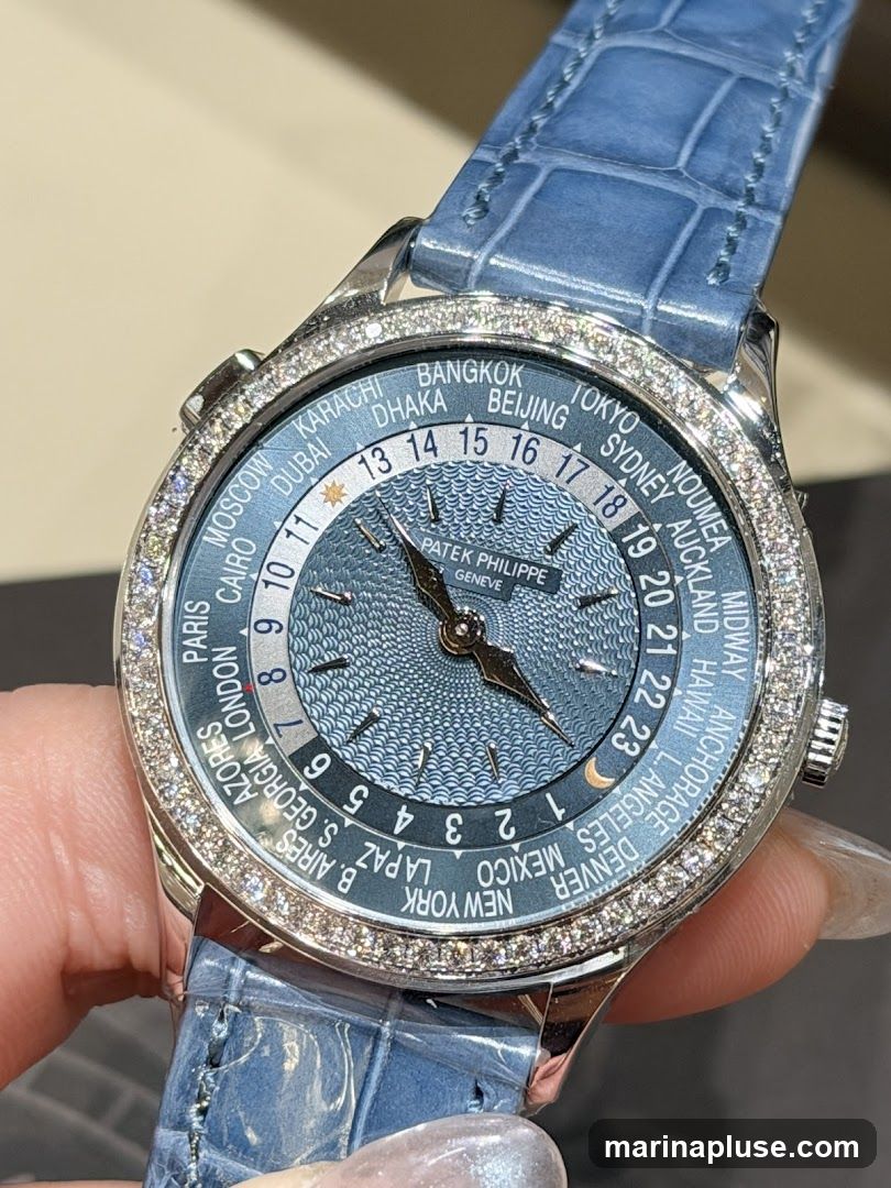 A close-up of a Patek Philippe World Time watch with a blue dial and a blue alligator leather strap. The bezel is encrusted with diamonds. The dial displays various city names around the world and a 24-hour ring.