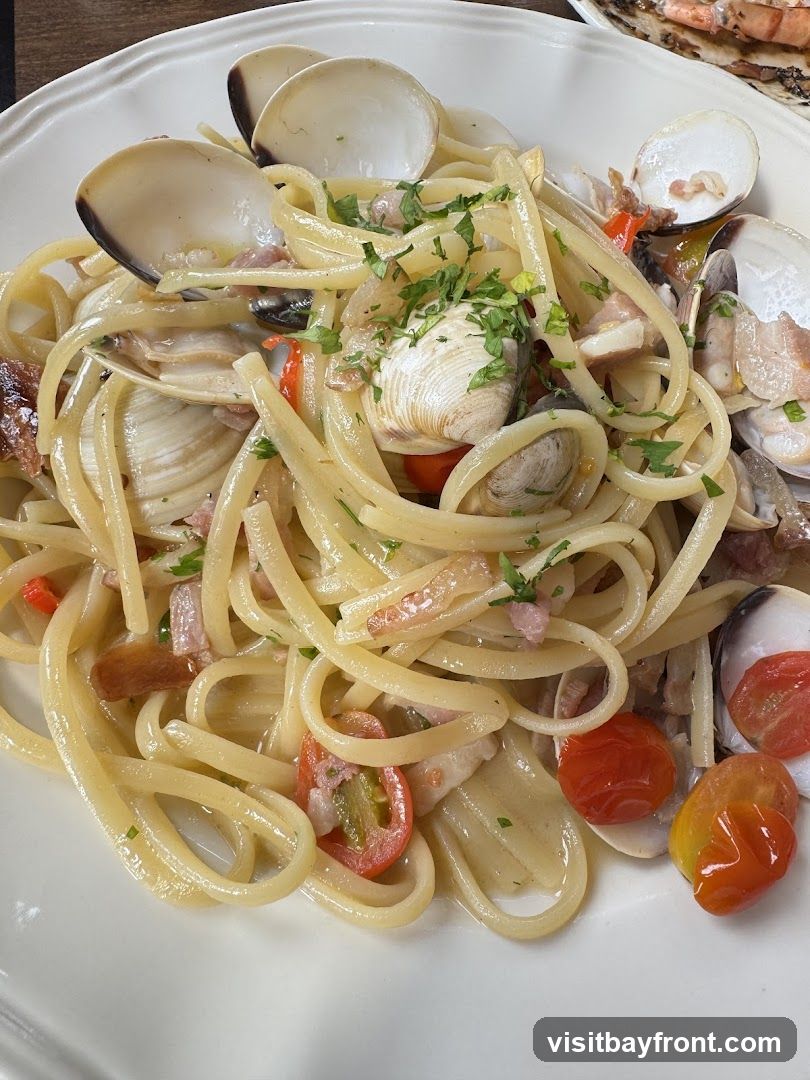 A close-up shot of linguine pasta with clams, cherry tomatoes, and herbs, served on a white plate.