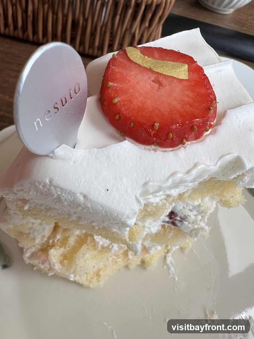 A slice of strawberry cake with white frosting and a strawberry on top. A silver disc with the word "nesuto" is inserted into the cake.
