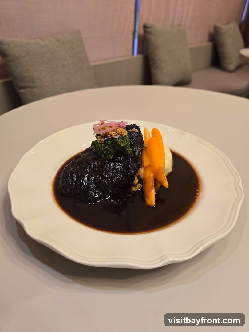 A plate of braised short ribs served with mashed potatoes, carrots, and a dark sauce. The dish is garnished with chopped greens and pickled red onions with mustard seeds. The setting appears to be a restaurant with upholstered seating in the background.