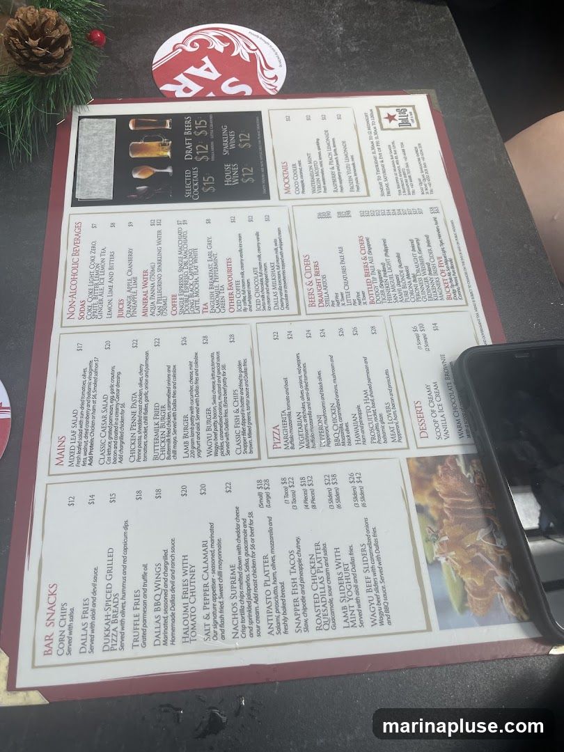 A menu from Dallas Bar with sections for Bar Snacks, Mains, Non-Alcoholic Beverages, Cocktails, Mocktails, Beers & Ciders, Pizza, Desserts, and Bottled Beers & Ciders.