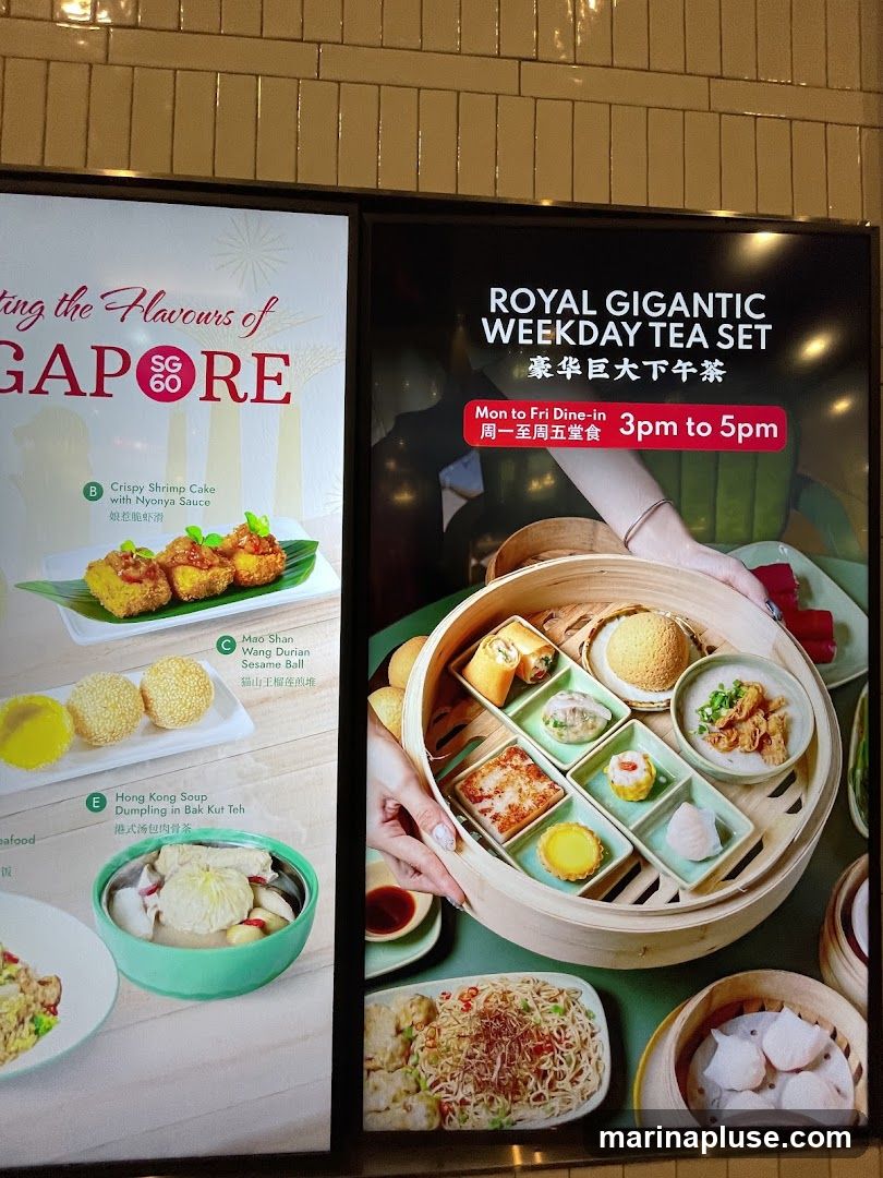 A digital display showing food promotions. The left side advertises "Flavours of Singapore" with items like Crispy Shrimp Cake and Hong Kong Soup. The right side promotes a "Royal Gigantic Weekday Tea Set" available Monday to Friday from 3pm to 5pm, featuring a selection of dim sum.