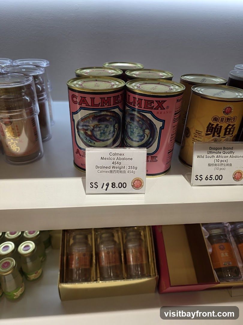 A shelf displaying various canned abalone products. In the foreground, there are cans of Calmex Mexico Abalone and Dragon Brand Wild South African Abalone. Below, there are gift boxes containing small bottles, possibly bird's nest soup.