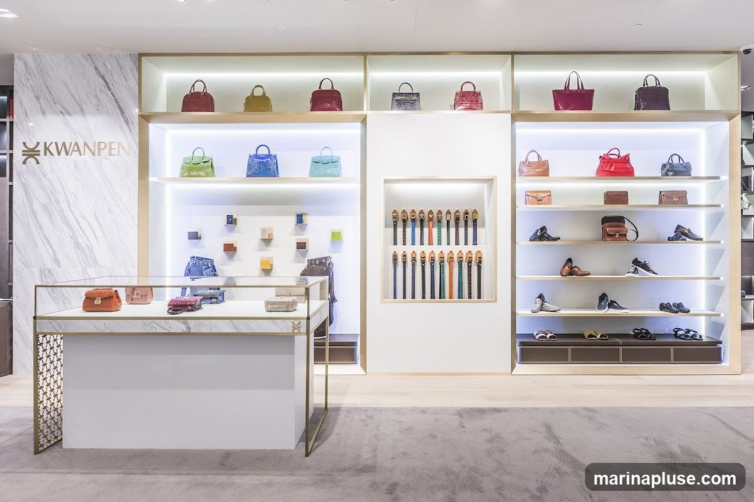 A well-lit interior display of a luxury store, featuring a variety of handbags, shoes, and belts. The walls are adorned with marble accents and illuminated shelving. The KWANPEN logo is visible on the left side of the display. A glass display case in the foreground showcases smaller leather goods.