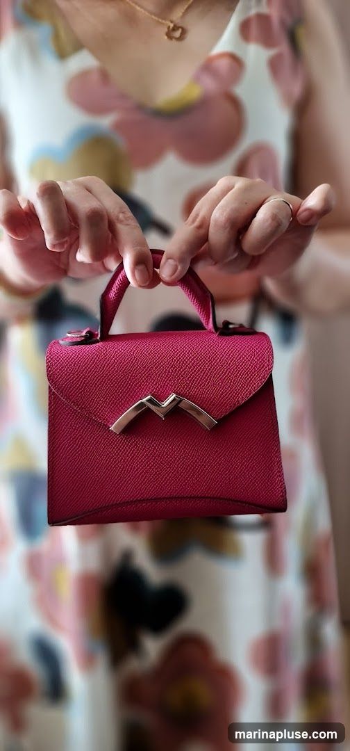 A woman is holding a small, textured pink handbag with a metallic clasp. She is wearing a dress with a floral pattern.