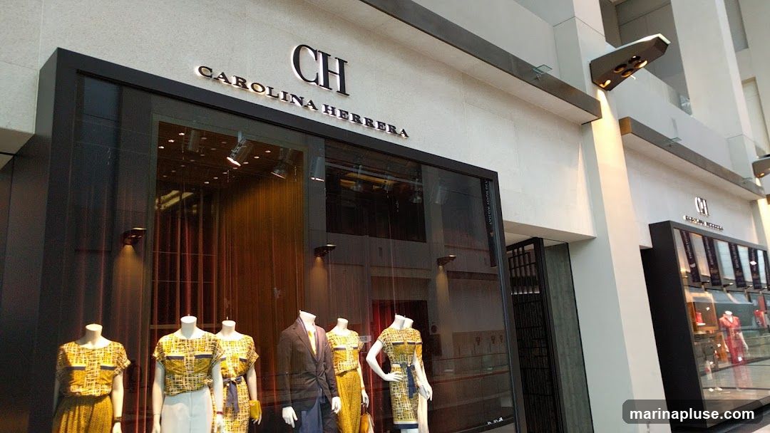 The exterior of a Carolina Herrera store with mannequins displaying clothing in the window. The store has a modern facade with large glass windows and prominent signage.
