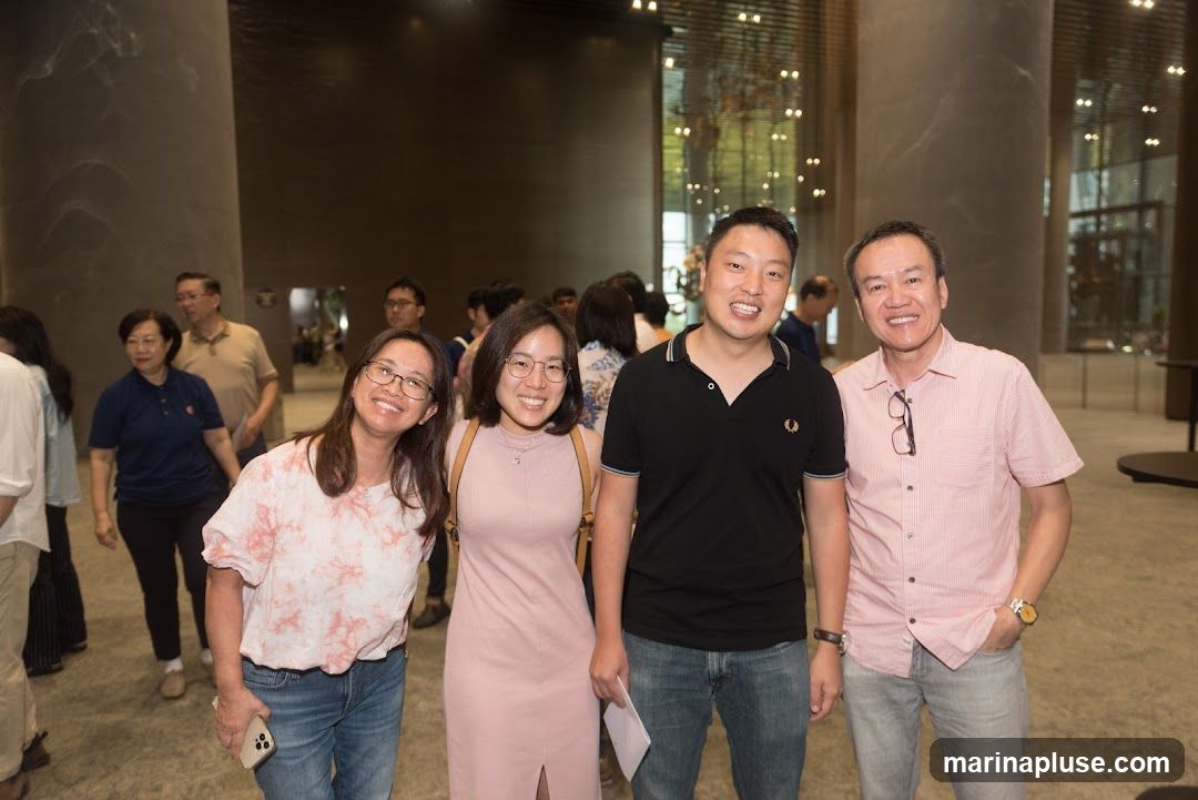 Four people, two women and two men, are posing for a photo in what appears to be a modern indoor space with large pillars and reflective ceilings. The two women are on the left, and the two men are on the right. They are all smiling and looking at the camera. The people are dressed casually. In the background, other people are visible, suggesting an event or gathering.