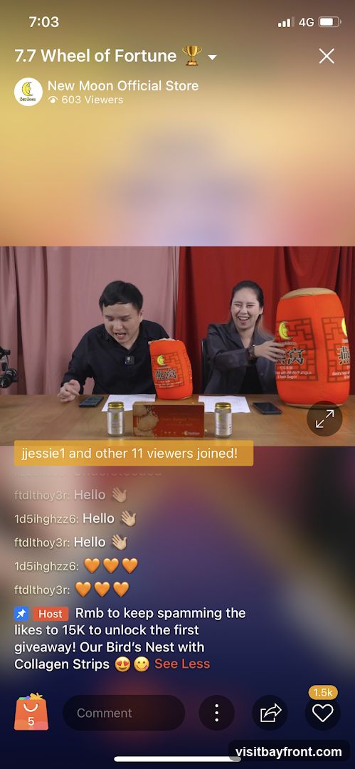 A live stream event titled "7.7 Wheel of Fortune" hosted by "New Moon Official Store". Two people are visible, with large orange cylindrical objects featuring Chinese characters and a moon logo. On the table are bottles and a box of what appears to be bird's nest product. A message indicates that "jjessie1 and other 11 viewers joined!". The host encourages viewers to spam likes to reach 15K for a giveaway of "Our Bird's Nest with Collagen Strips". The stream has 603 viewers and 1.5K likes.