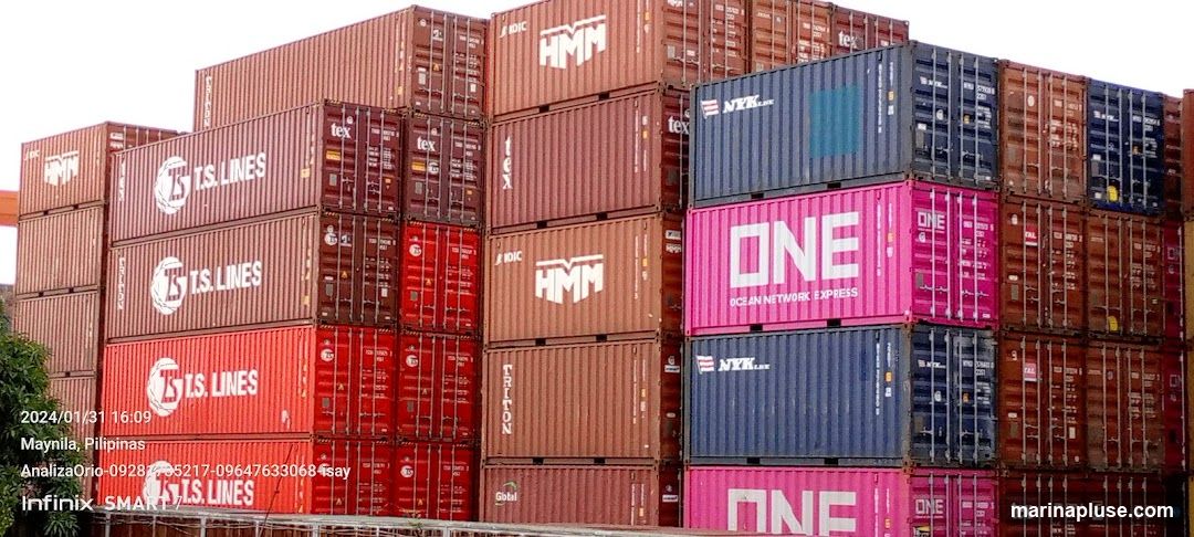 A large stack of shipping containers of various colors including red, brown, blue, and pink. Some containers have company logos such as T.S. LINES, HMM, ONE (Ocean Network Express), and NYK. The image also includes a timestamp and location information at the bottom left.