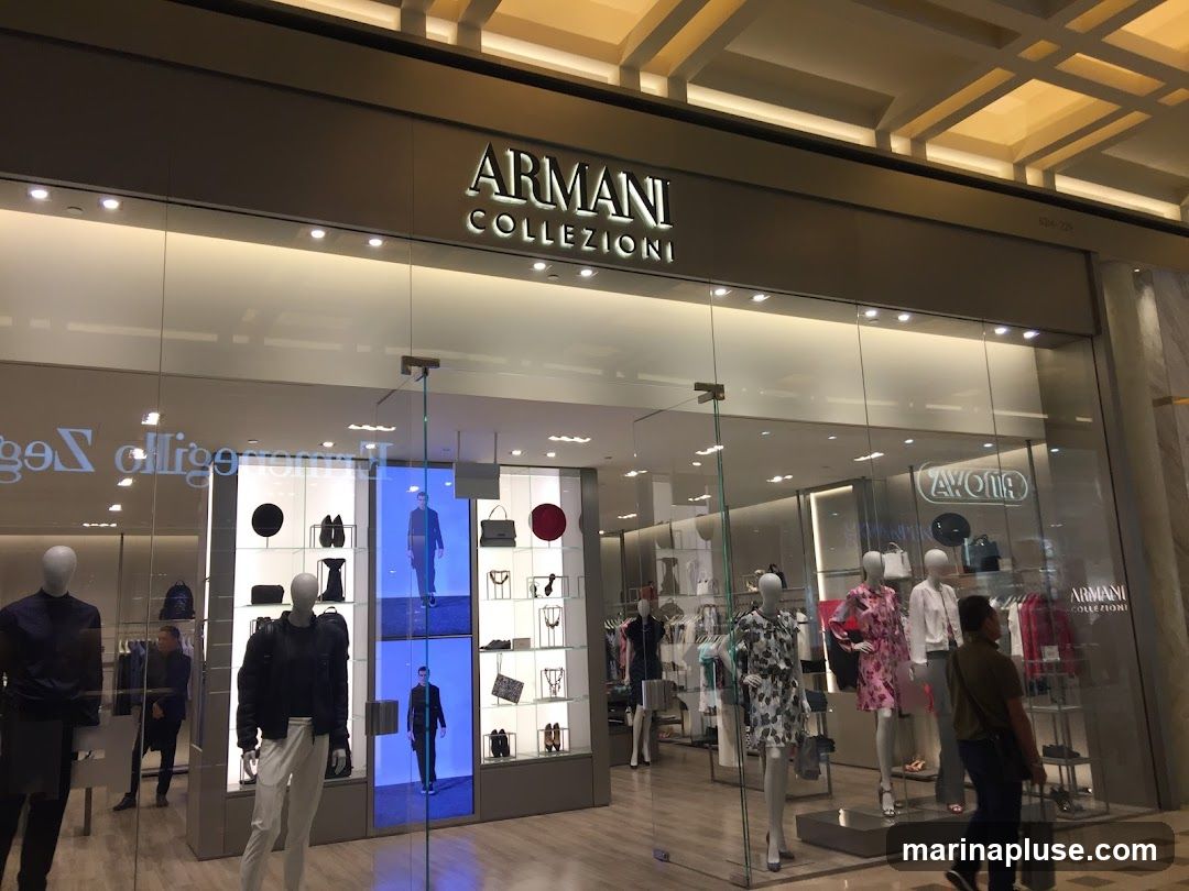 The exterior of an Armani Collezioni store. The store has a large glass facade with mannequins displaying clothing inside. The Armani Collezioni logo is prominently displayed above the entrance.