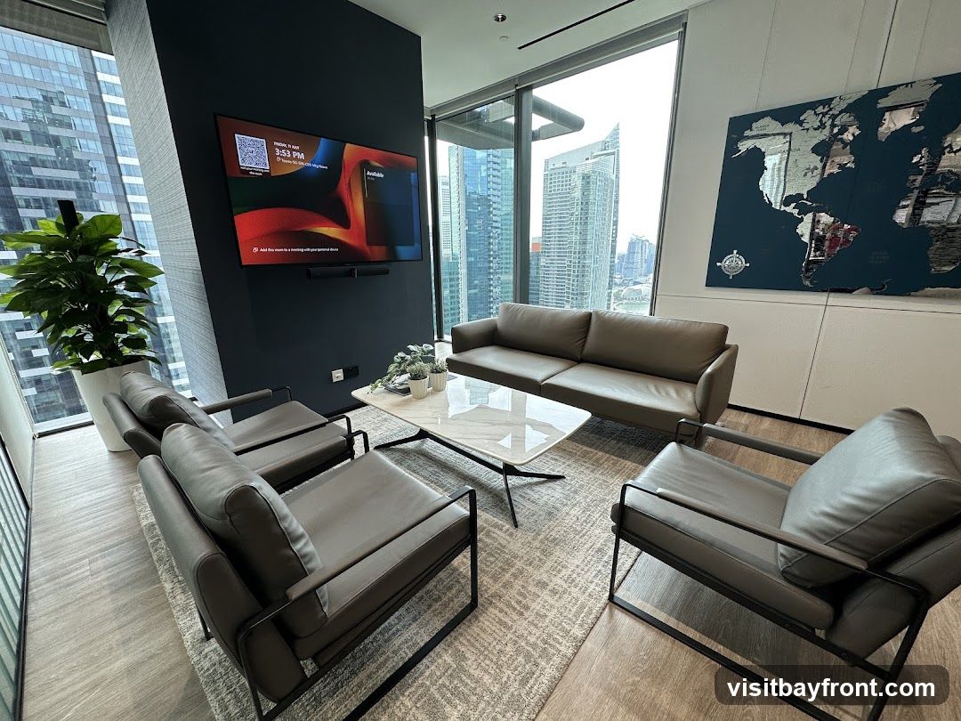 A contemporary waiting area with a large window offering a city view. The room features a dark grey accent wall with a mounted television displaying a calendar and a QR code. There are two grey leather sofas and four matching armchairs arranged around a white marble coffee table. A large world map artwork hangs on the adjacent wall. A tall potted plant adds a touch of greenery to the space.