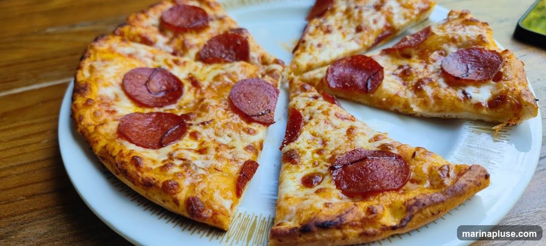 Several slices of pepperoni pizza are arranged on a white plate with a decorative rim. The pizza has a golden-brown crust, melted cheese, and round slices of pepperoni. The plate is placed on a wooden surface.