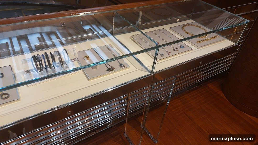 A glass display case filled with various jewelry items, including bracelets, necklaces, and rings. The case has a mirrored base and is set on a polished wooden floor.