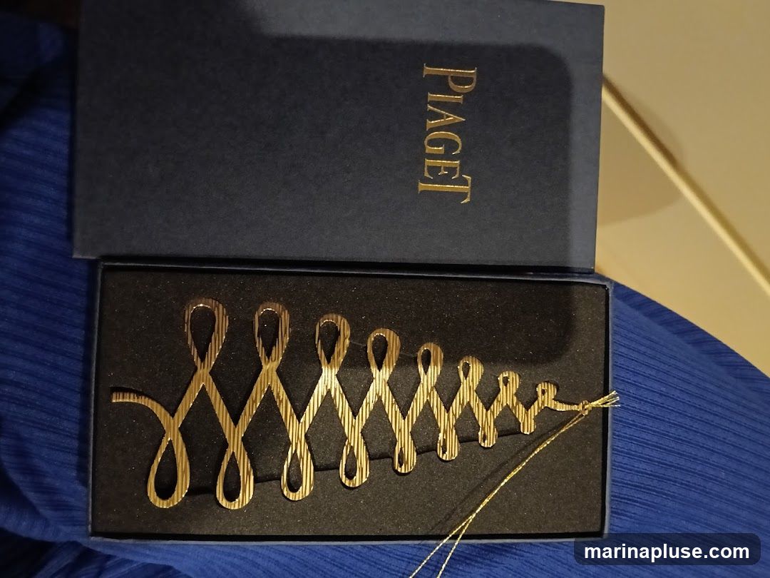 A gold-colored ornament in the shape of a stylized Christmas tree is displayed in a dark blue Piaget box. The ornament has a textured surface and a thin gold string attached. The Piaget logo is embossed in gold on the lid of the box.