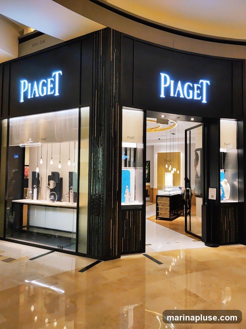 The exterior of a Piaget store, featuring illuminated signage above a glass storefront. Inside, display cases showcase watches and jewelry. The store has a modern and luxurious design with dark wood accents and polished floors.