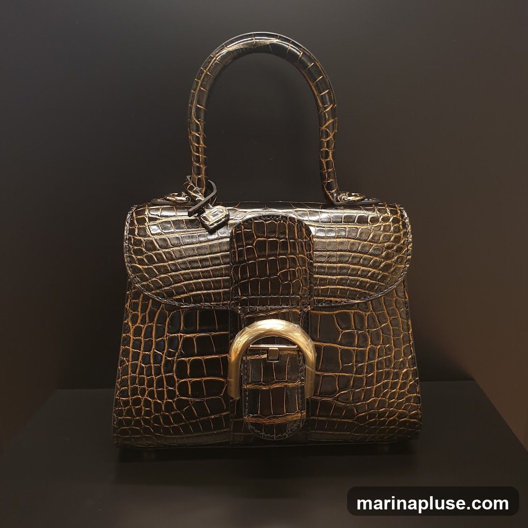 A close-up studio shot of a brown crocodile-embossed leather handbag with gold hardware. The bag has a top handle and a flap closure with a distinctive gold buckle. The texture of the crocodile embossing is prominent, and the bag is set against a dark, plain background.
