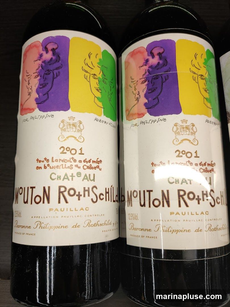 Two bottles of Chateau Mouton Rothschild 2001 Pauillac wine are displayed. The labels feature a colorful artistic design with portraits and the text "FOR PHILIPPINE" and "ROBERT WILSON". Below this, the vintage "2001" is prominent, followed by details about the wine being bottled at the chateau. The main label reads "CHATEAU MOUTON ROTHSCHILD" with "PAUILLAC" and "APPELLATION PAUILLAC CONTROLEE". The producer is listed as "Baronne Philippine de Rothschild".