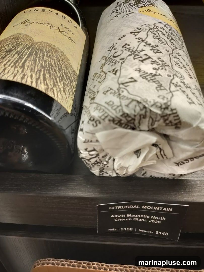 Two bottles of wine are displayed on a shelf. The bottle on the left has a label that reads "VINEYARDS Magnetic North 2020". The bottle on the right is wrapped in paper with a map-like pattern. A price tag below the bottles indicates "CITRUSDAL MOUNTAIN Alheit Magnetic North Chenin Blanc 2020" with a retail price of $158 and a member price of $148.