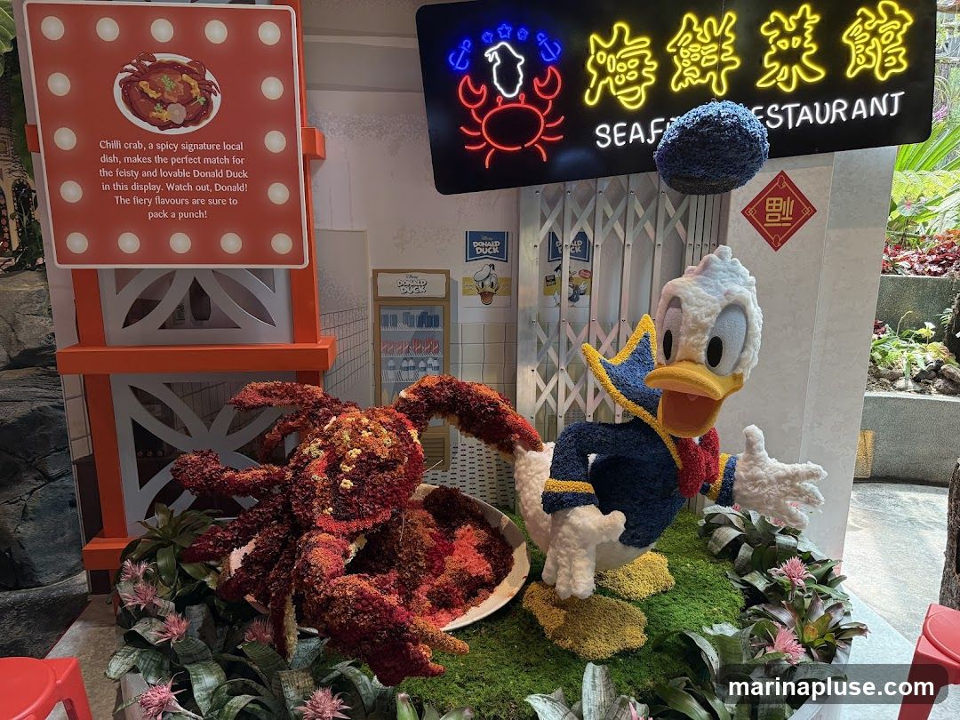 A display featuring a floral sculpture of Donald Duck next to a floral sculpture of a crab. A sign describes chilli crab as a spicy local dish. A neon sign reads "SEAFOOD RESTAURANT" in English and Chinese.