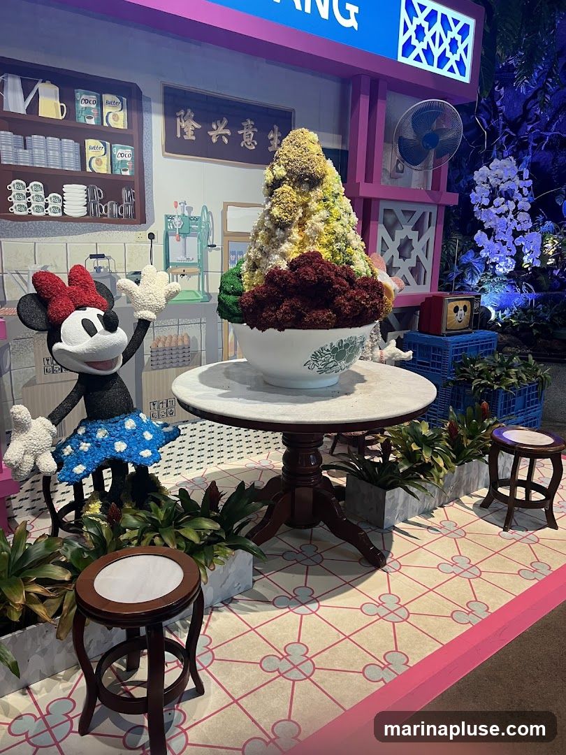 A whimsical display featuring a large, colorful dessert resembling shaved ice, a Minnie Mouse figure, and a backdrop designed to look like a traditional shop. The backdrop includes shelves with mugs and cans, a vintage ice shaver, and a sign with Chinese characters. The floor has a patterned design with Mickey Mouse motifs.