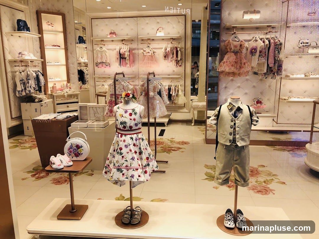 A brightly lit children's clothing store display featuring mannequins dressed in formal and casual wear. The display includes racks of dresses, shirts, and pants, as well as shoes and accessories. The store's interior is decorated with floral patterns on the floor and walls.