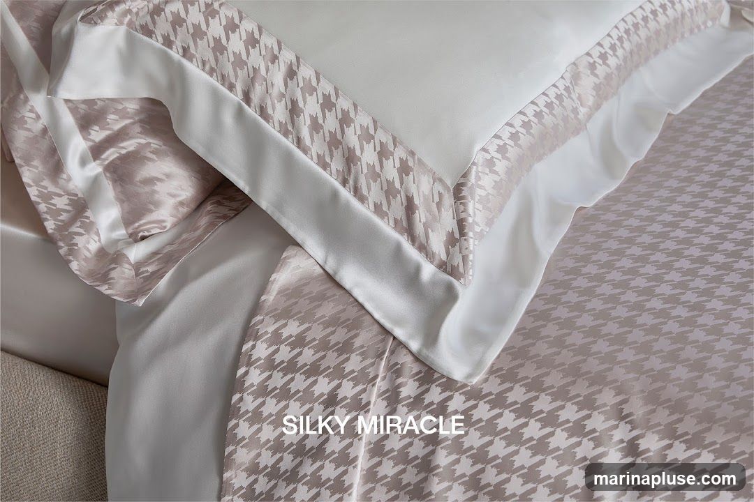 A close-up view of luxurious bedding with a houndstooth pattern. The bedding appears to be made of silk and features a white trim. The text "SILKY MIRACLE" is visible on the fabric.