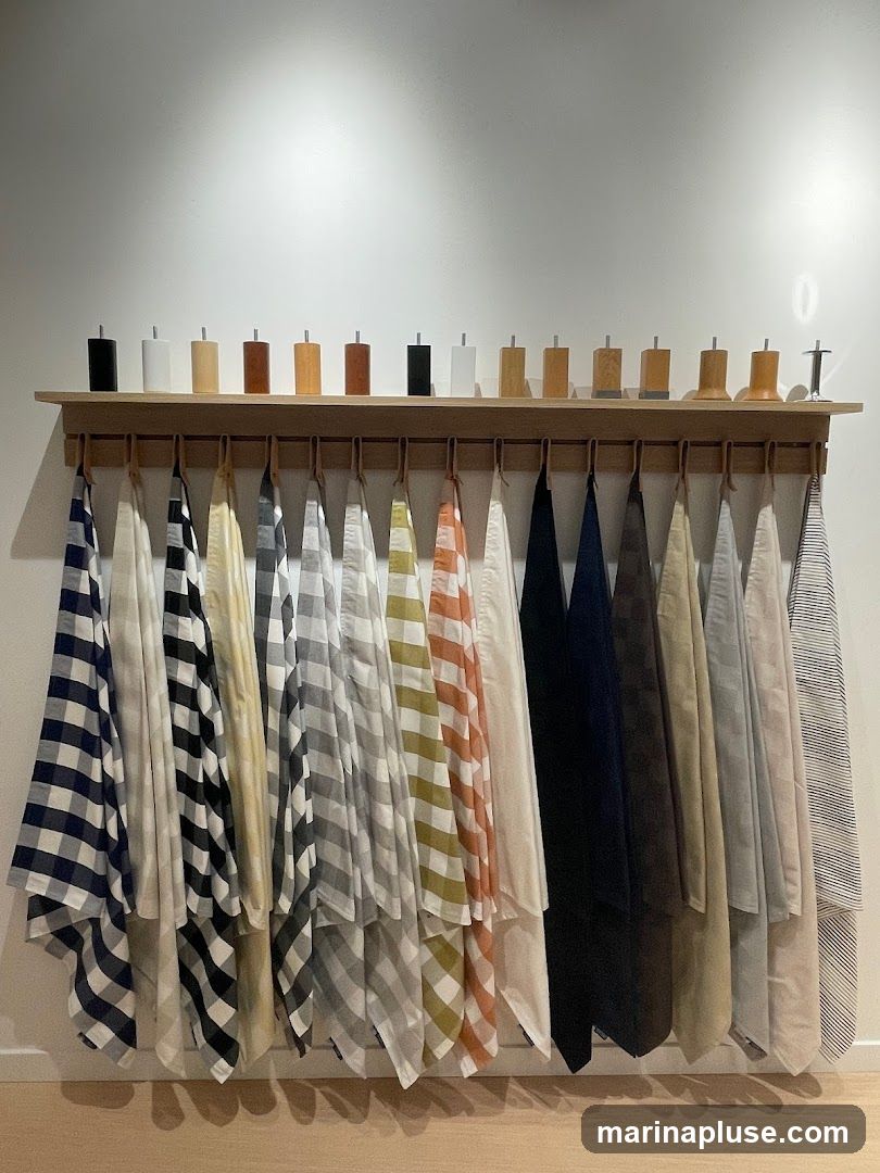 A wooden shelf displays various fabric samples hanging below. Above the shelf, a row of wooden blocks with metal tops are arranged. The fabrics are in different patterns and colors, including gingham, stripes, and solid colors.