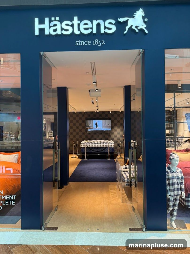 The entrance to a Hästens store, featuring the brand's logo and name above the doorway. The store displays beds and bedding, with a mannequin dressed in pajamas visible to the right.