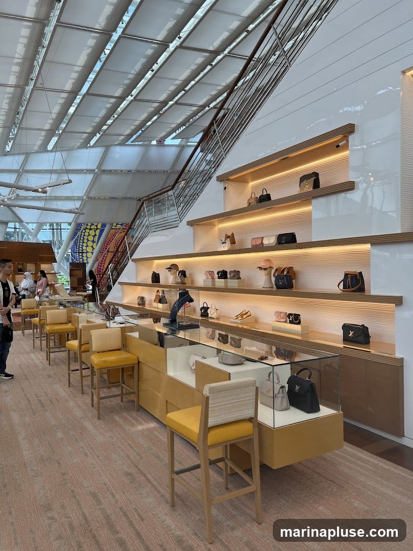A well-lit interior of a luxury retail store, showcasing a variety of handbags on shelves and in display cases. The store features a modern design with a sloped ceiling, a staircase, and minimalist furniture. Several customers are browsing the merchandise.