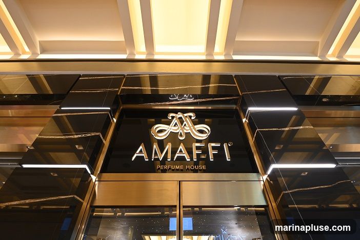 The exterior of a luxury perfume shop with a black marble facade and gold accents. The shop's name, "AMaffi PERFUME HOUSE," is displayed prominently in gold lettering above the entrance. The entrance features large glass doors.