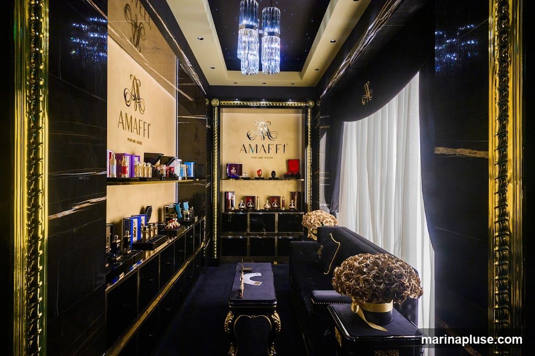 The interior of a luxurious perfume shop with black marble walls, gold accents, and crystal chandeliers. Display shelves are filled with various perfume bottles. A black velvet sofa and ornate tables are arranged for seating.