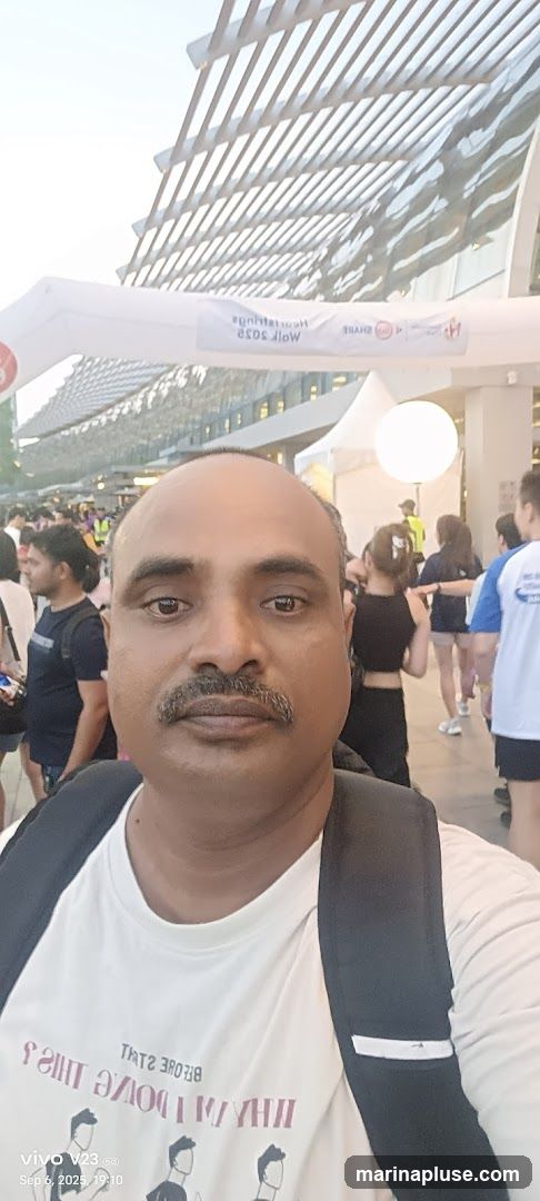 A man takes a selfie in front of a crowd at an outdoor event. Behind him, there is a white archway with text that appears to be for a race or event. The text on the archway is partially obscured and reversed, but some words like "Heritage" and "Race" are visible. There are also logos on the archway. In the background, people are milling around, and there is a large, illuminated sphere. The man is wearing a white t-shirt with a graphic and text that reads "THINGS I DO BEFORE I SLEEP". The date and time stamp "vivo V23 5G Sep 6, 2025, 19:10" is visible in the bottom left corner.