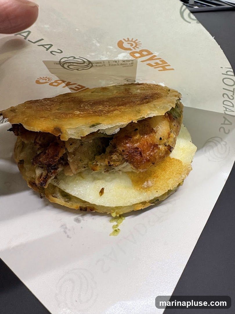 A close-up shot of a sandwich, possibly chicken, with melted cheese and green sauce, wrapped in branded paper. The paper has the logo and text "HEABO" and "SALAD" visible.