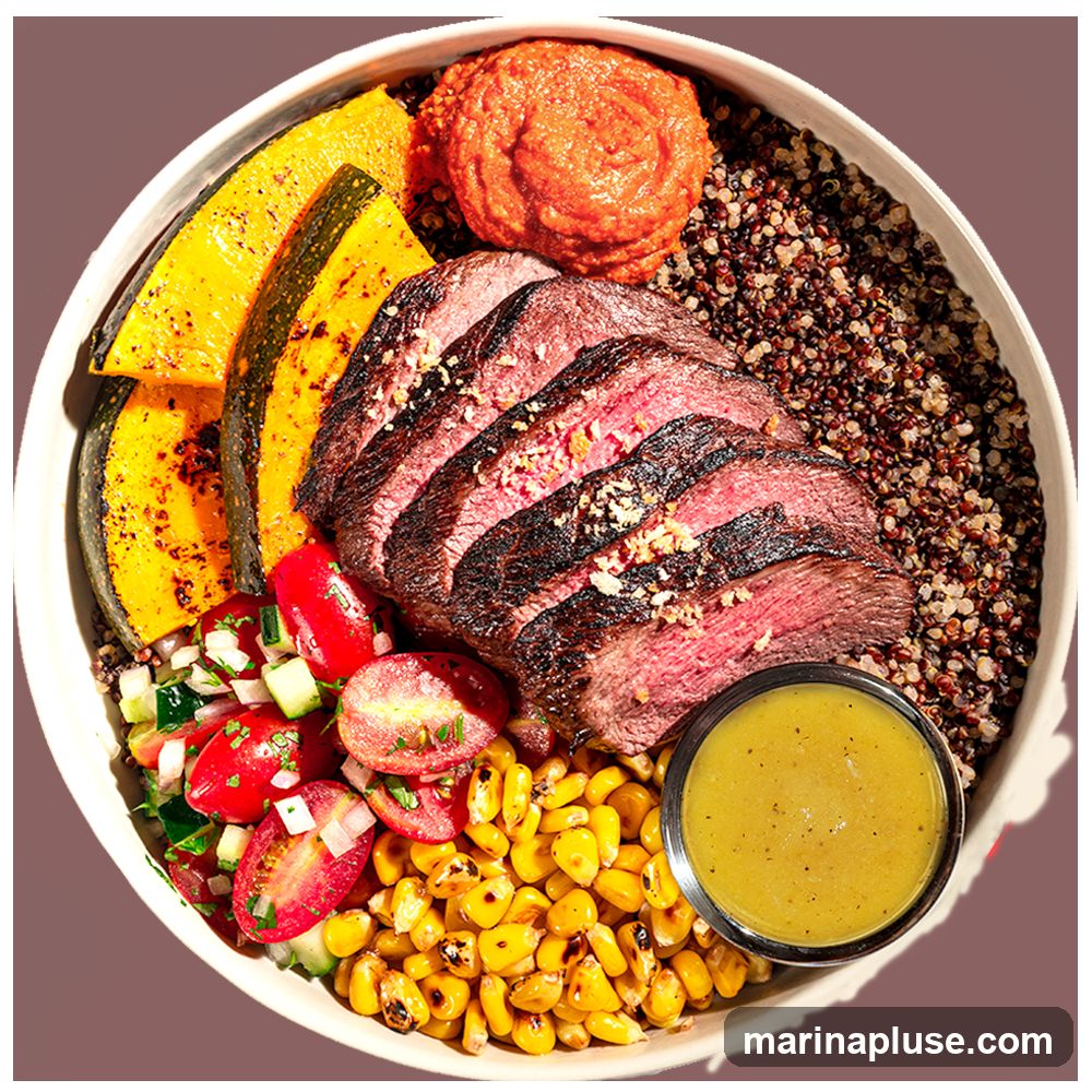 A close-up overhead shot of a steak and quinoa bowl. The bowl contains sliced grilled steak, roasted squash, corn, a tomato and cucumber salad, a dollop of red pepper spread, and a small dish of yellow dressing. The base of the bowl appears to be quinoa.