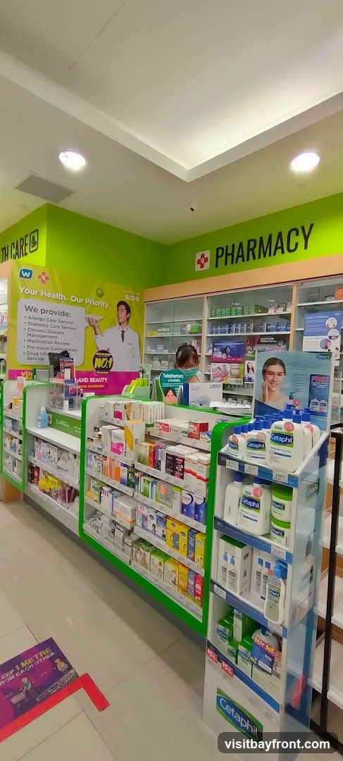 The interior of a brightly lit pharmacy with shelves stocked with various health and beauty products. Prominent signage indicates "HEALTH CARE" and "PHARMACY". A display features Cetaphil skincare products. A floor sticker reminds customers to "KEEP 1 METRE FROM EACH OTHER".