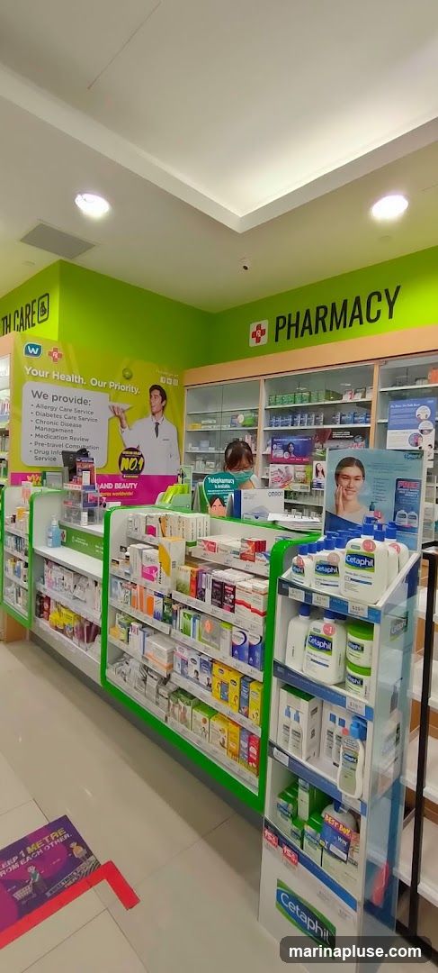 The interior of a brightly lit pharmacy with shelves stocked with various health and beauty products. Prominent signage indicates "HEALTH CARE" and "PHARMACY". A display features Cetaphil skincare products. A floor sticker reminds customers to "KEEP 1 METRE FROM EACH OTHER".