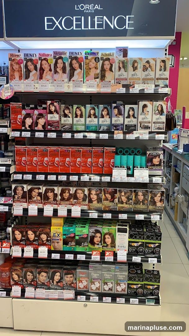 A retail display featuring various shades of L'Oréal Excellence hair color products. The top shelf showcases different shades like Rose, Dusty, Sahara, Metallic, Primer, and Khaki, with prices listed below. The subsequent shelves display more hair color boxes from brands like L'Oréal, Revlon, and Bigen, along with other hair care products. Prices are visible for many items.