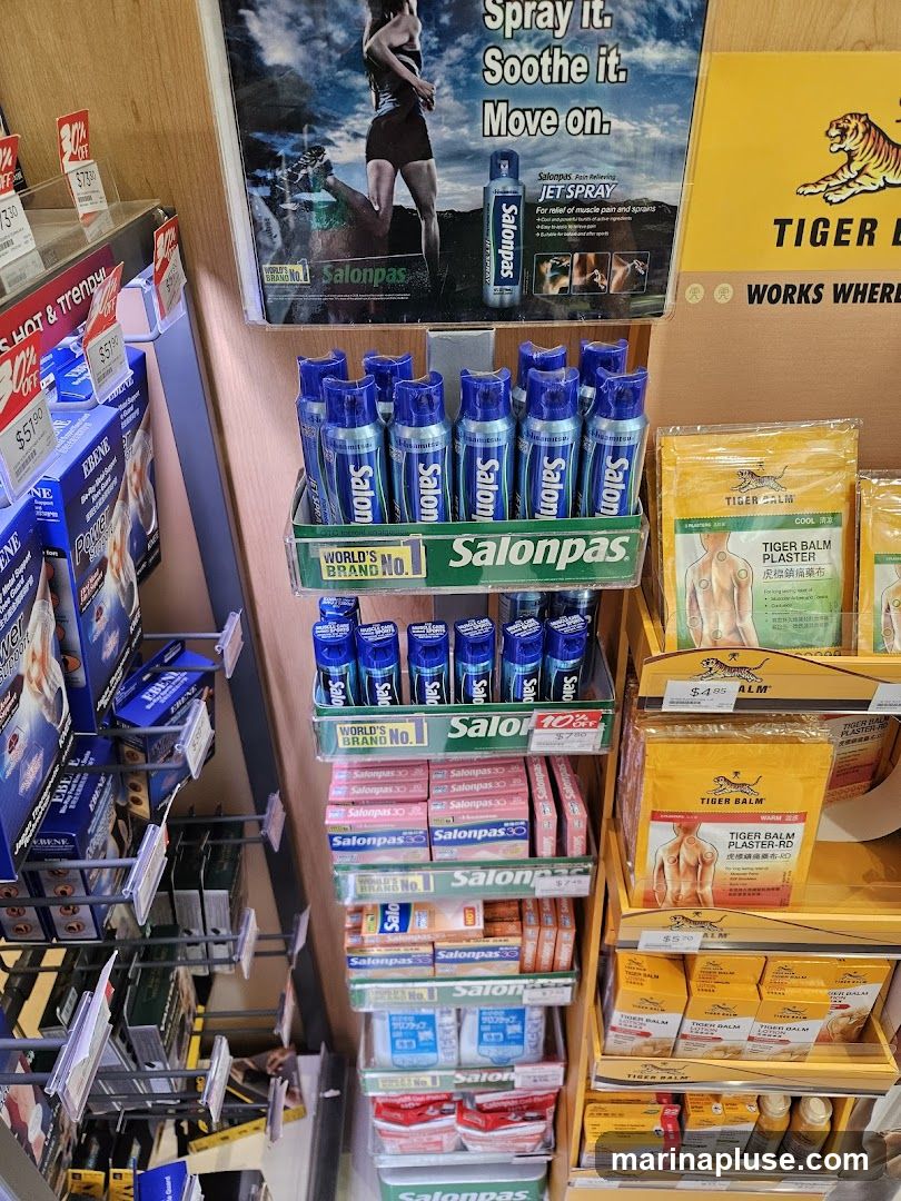 A retail display featuring various pain relief products, including Salonpas jet spray, plasters, and Tiger Balm products. The display includes promotional posters and product packaging.