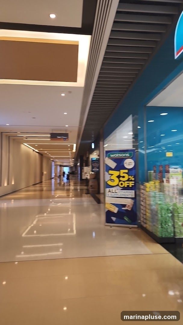 A view down a brightly lit shopping mall corridor. On the right, a Watsons store is visible with a large blue and white banner advertising "35% OFF ALL VITAMINS & SUPPLEMENTS". Products are displayed behind the glass window.