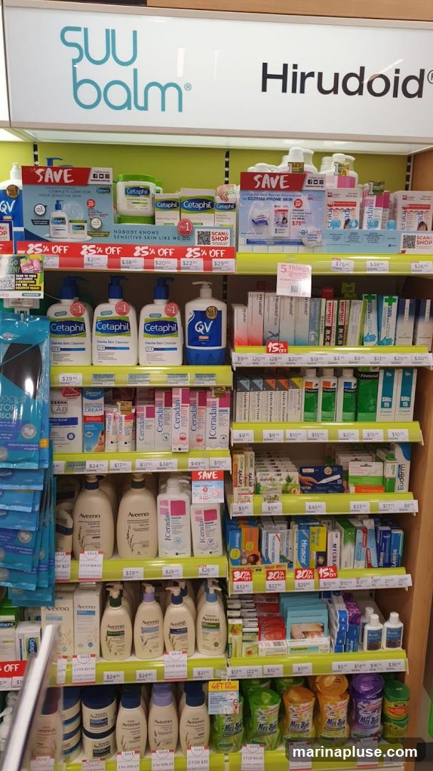 A retail display featuring a variety of skincare products, including brands like Cetaphil, QV, Aveeno, and Ceradan. Many products are displayed with promotional signage indicating discounts such as "SAVE" and "25% OFF". The shelves are organized with different product types, from cleansers and moisturizers to creams and lotions. Prominent branding for "SUU balm" and "Hirudoid" is visible at the top of the display.