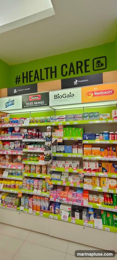 A well-lit interior view of a pharmacy or health store, showcasing shelves stocked with a wide variety of health and wellness products. Prominent signage includes "#HEALTH CARE" in large black letters on a bright green background, with smaller labels for "Children's Health" and "Probiotics." Various brands like Swisse, BioGaia, Redoxon, Scotts, and Centrum are visible. The shelves are organized with vitamins, supplements, and other health-related items, many with price tags and promotional labels.