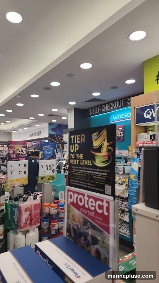 The image shows the interior of a Watsons store, with various health and beauty products on display. Signs indicate "Self-Checkout" and "#Haircare". Promotional posters are visible, including one titled "Tier Up to the Next Level" and another with the text "Protect yourself & your loved ones". Several product displays and shelves are filled with items like lotions, vitamins, and other personal care products.