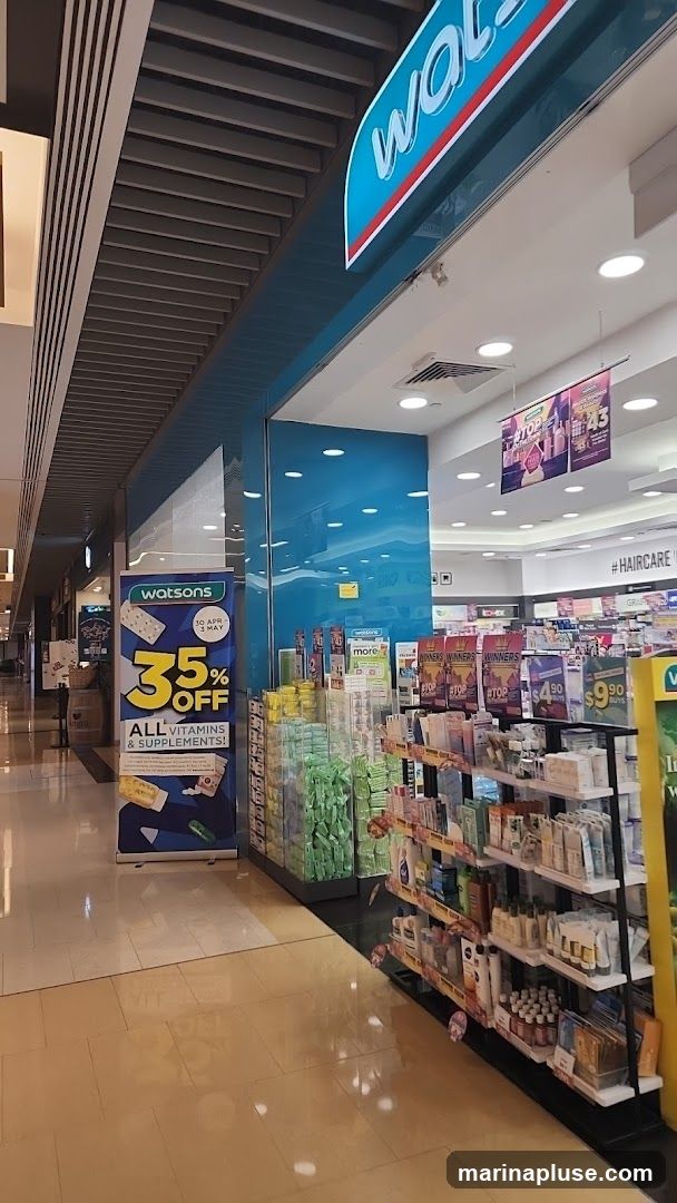 A view of a Watsons store with its prominent blue and white signage visible. Inside, shelves are stocked with various health and beauty products. A promotional banner outside advertises 35% off all vitamins and supplements.