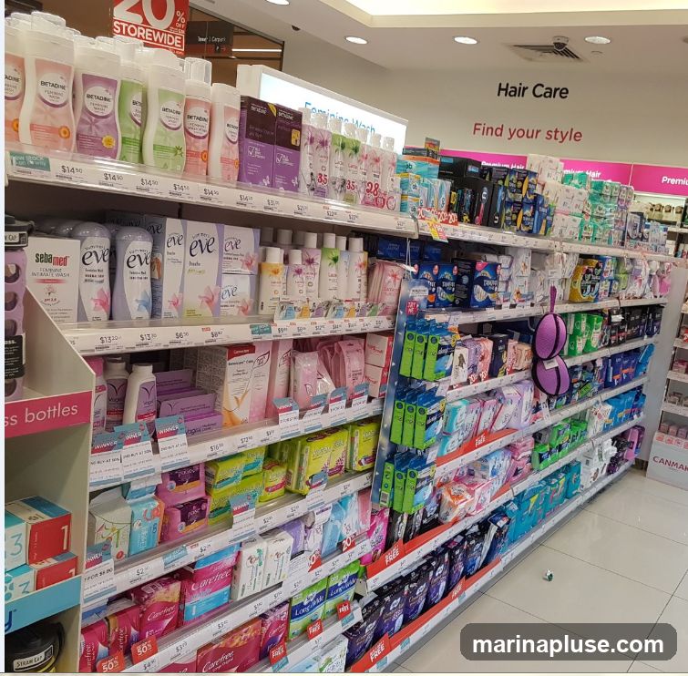 Aisle in a store featuring feminine wash products, sanitary pads, and hair care items. The shelves are stocked with various brands and sizes of products, with price tags visible. A sign for "Hair Care" and "Find your style" is displayed on the wall.