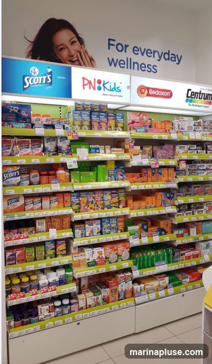 Shelves stocked with various brands of vitamins and supplements, including Scott's, PN Kids, Redoxon, and Centrum. The display features promotional signage and product packaging.