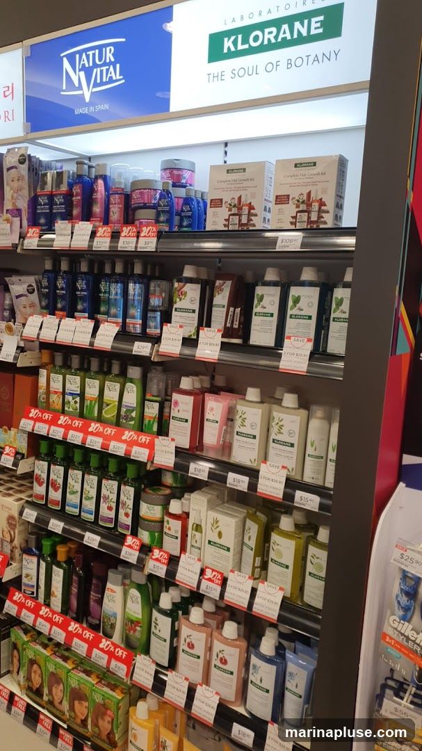 A retail display featuring various skincare and haircare products from brands like Natur Vital and Klorane. The shelves are stocked with bottles, boxes, and jars of lotions, shampoos, conditioners, and hair growth kits. Promotional signs indicating discounts like "20% OFF" and "SAVE" are visible.
