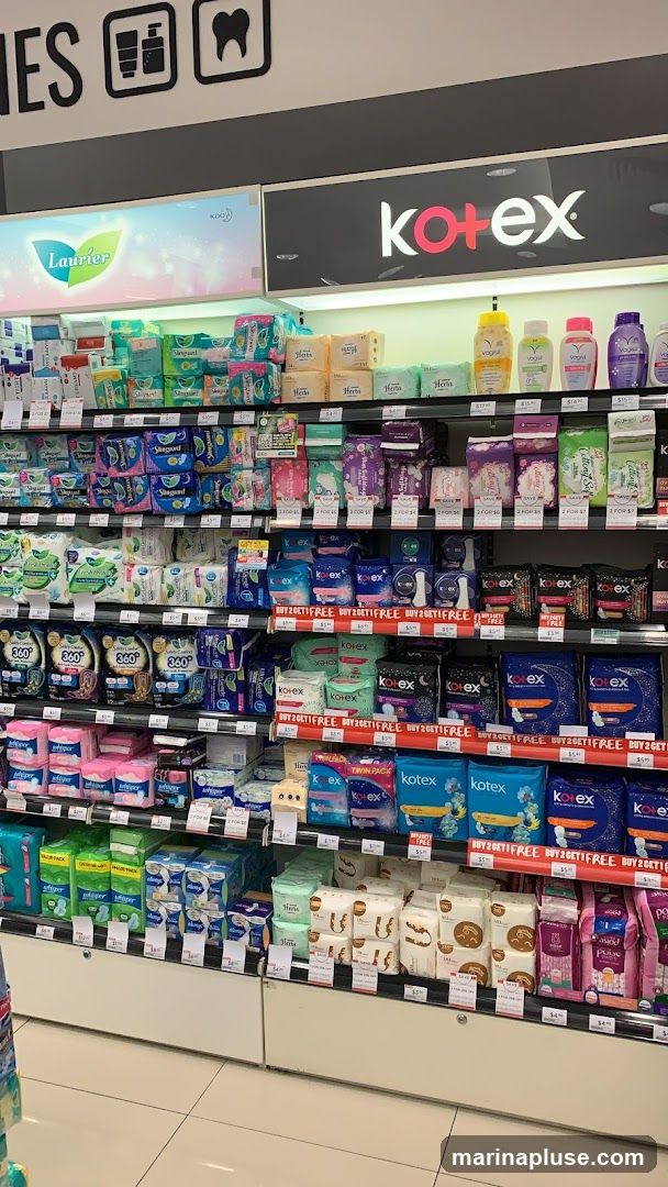 A retail display featuring a wide selection of feminine hygiene products, including sanitary pads and panty liners, from various brands such as Kotex, Laurier, Whisper, and 360°. The products are neatly arranged on shelves with visible pricing and promotional signage.