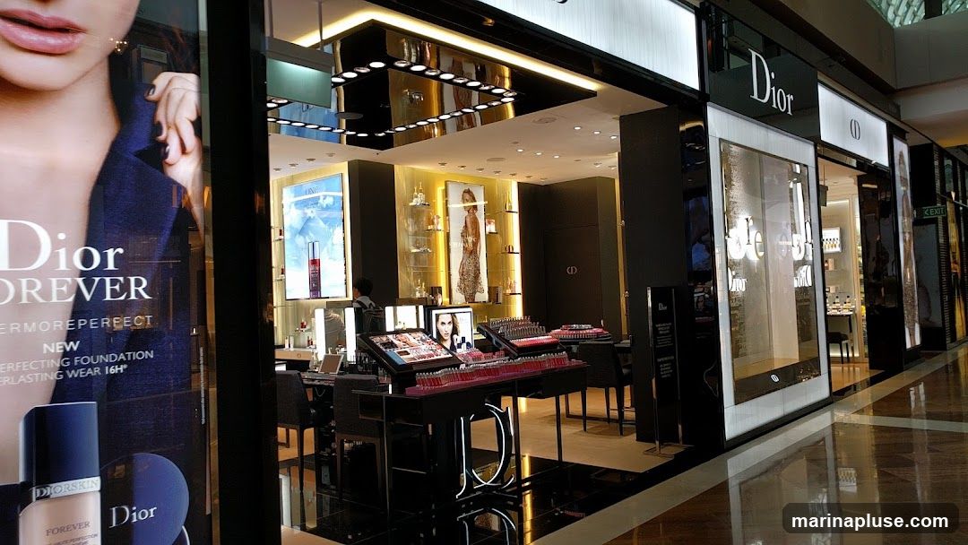 The exterior of a Dior store, featuring large displays of makeup and skincare products. A prominent advertisement for Dior Forever foundation is visible on the left. The store's signage and illuminated displays are clearly visible.