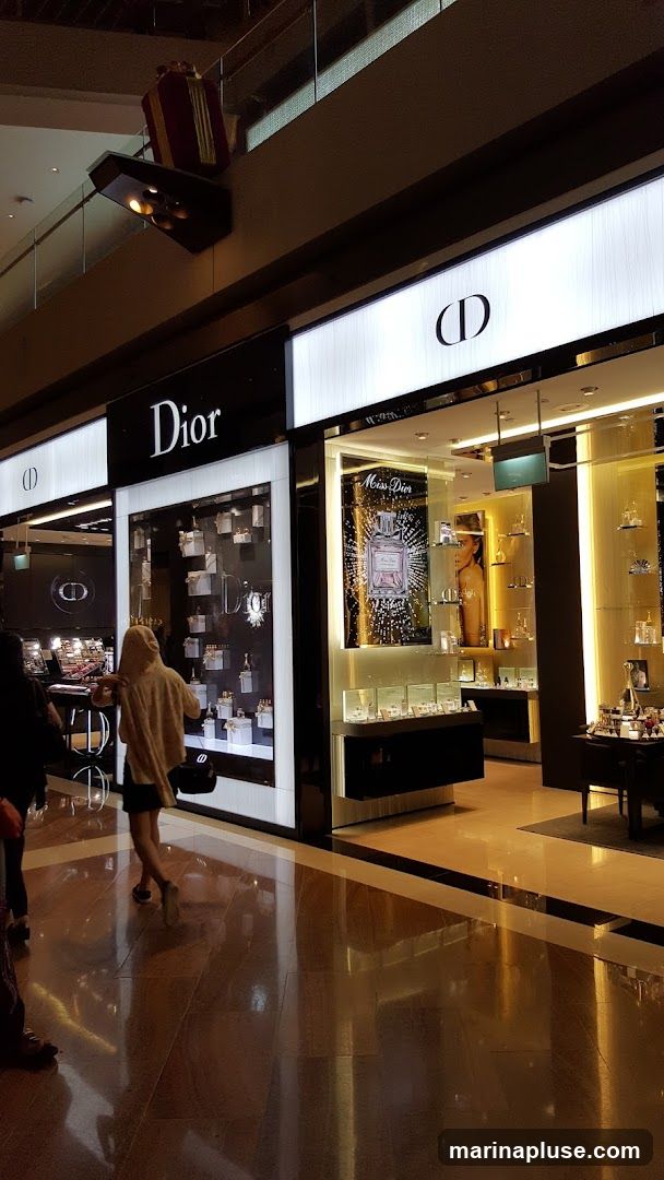 The exterior of a Dior store with illuminated signage and display windows showcasing perfumes and cosmetics. A large advertisement for Miss Dior perfume is visible.