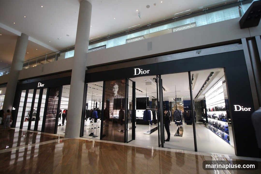 The exterior of a Dior store in a mall. The store has large glass windows displaying clothing and accessories. The Dior logo is visible above the entrance.